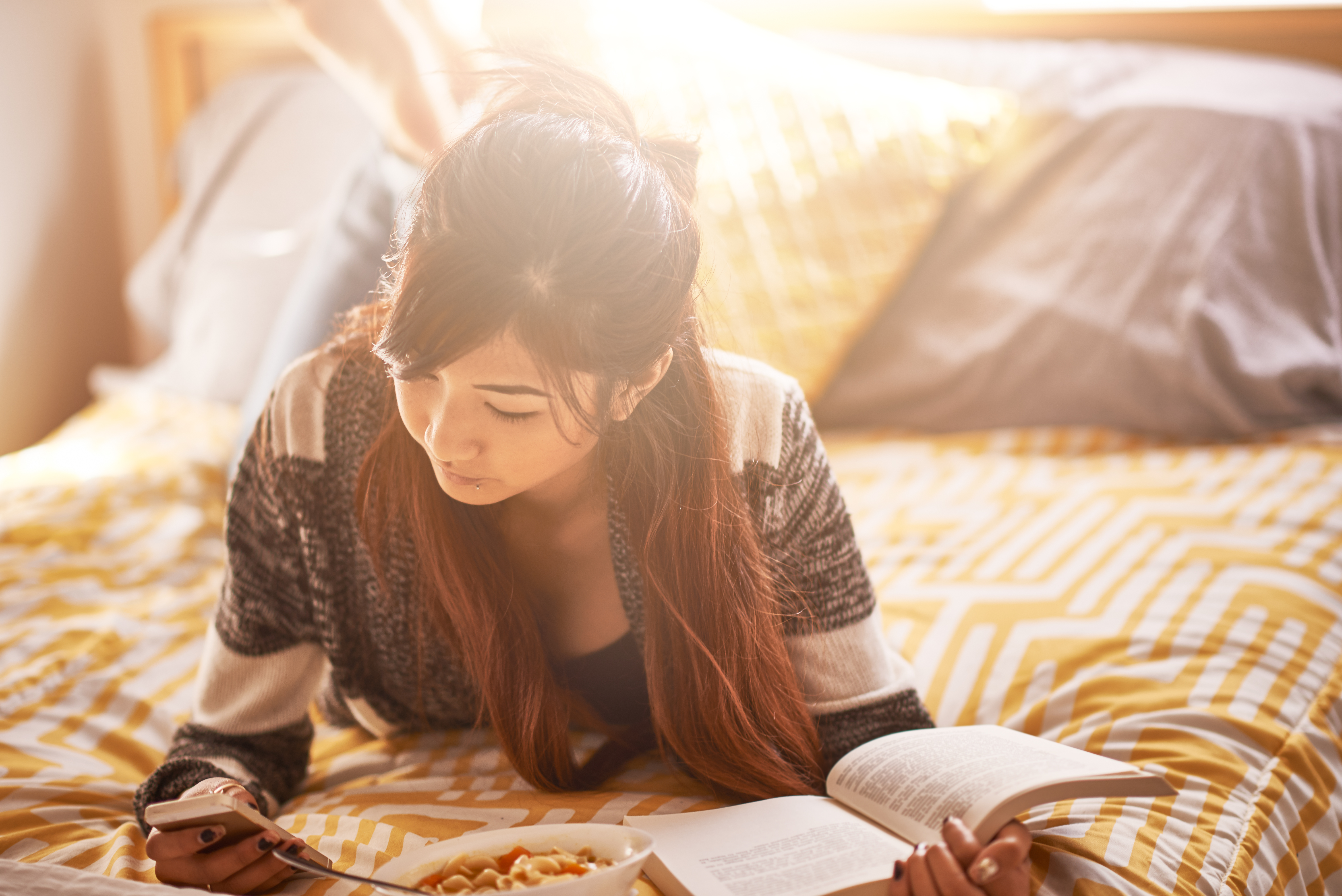 asian-teen-checking-smartphone-while-reading-book-and-eating-soup-524228629_6016x4016.jpeg